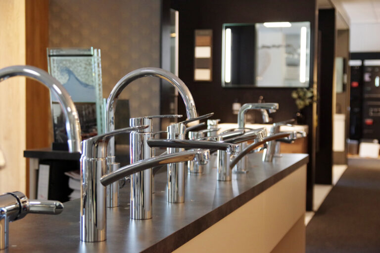 Showroomopstelling met diverse moderne chromen keuken- en badkamerkranen gepresenteerd op een donker werkblad
