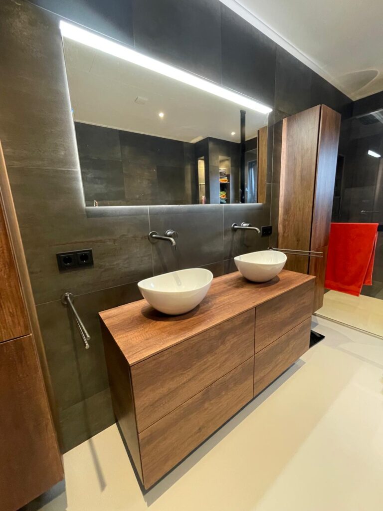 Luxe badkamer met dubbel houten wastafelmeubel, twee opzetwaskommen, wandkranen en grote spiegel met geïntegreerde LED-verlichting