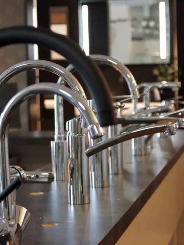 Showroom met moderne keuken- en badkamerkranen in diverse stijlen, waaronder matzwart en chroom, gepresenteerd op een donker werkblad