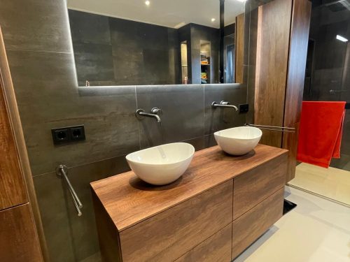 d6524d53-c45c-4280-98a1-45e330ea6f0f Luxe badkamer met dubbel houten wastafelmeubel, twee opzetwaskommen, wandkranen en grote spiegel met geïntegreerde LED-verlichting